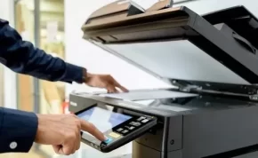Persona utilizando una impresora multifuncional para realizar copias o escanear un documento en una oficina.